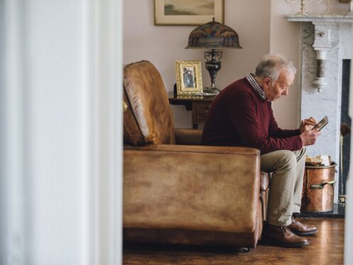 Senior man is sitting in an armchair in the living room of his home.